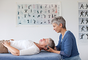 Eine Therapeutin behandelt eine Patientin, die auf dem Rücken liegt, im Nackenbereich.